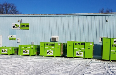Industrial waste containers from a dumpster rental franchise lined up outside a blue building with contact information on both containers and building.