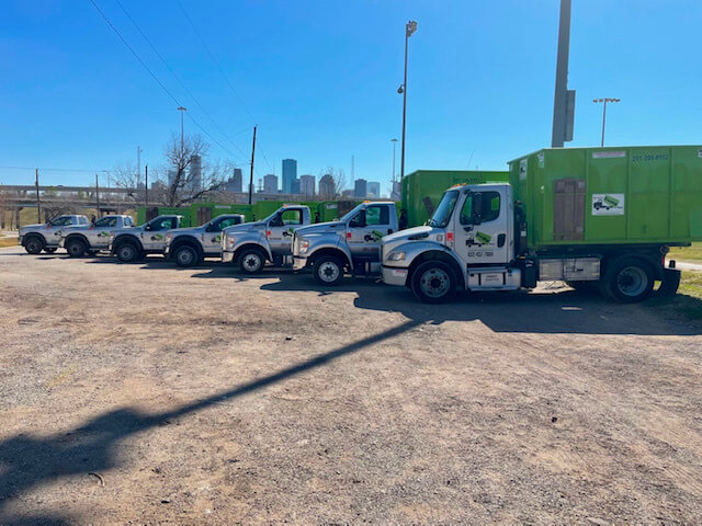 A fleet of junk removal franchise trucks parked in a line with a city skyline.