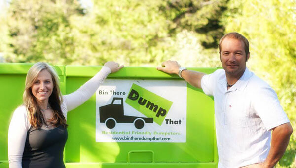 Two people standing next to a green dumpster, part of the "bin there dump that" junk removal franchise.