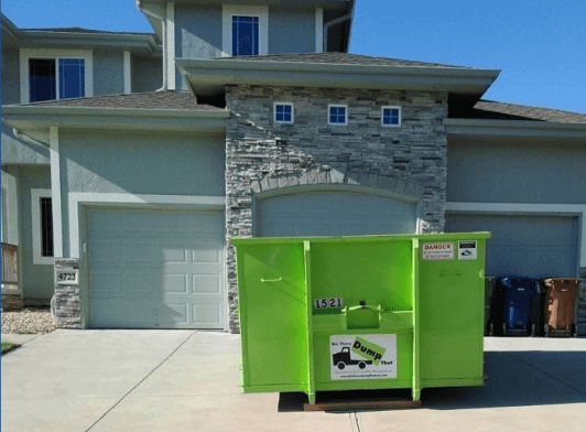 A bright green dumpster rental franchise in front of a two-story house with stone accents.