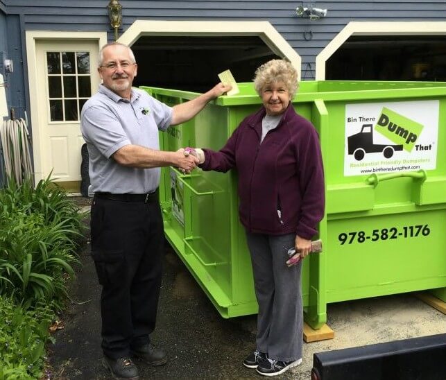 Two individuals shaking hands in front of a green dumpster from the junk removal franchise "bin there dump that.