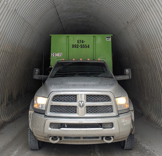 A junk hauling franchise pickup truck towing a trailer stuck in a narrow tunnel.