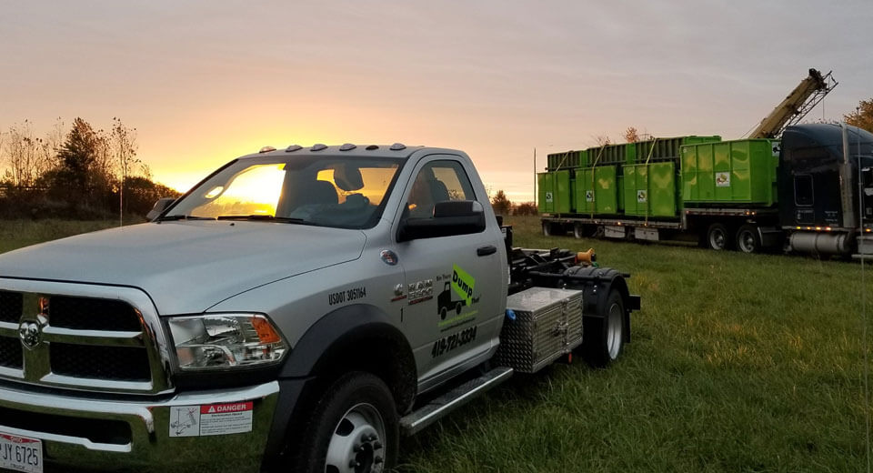 A junk removal franchise truck is parked in front of a trailer at sunset.