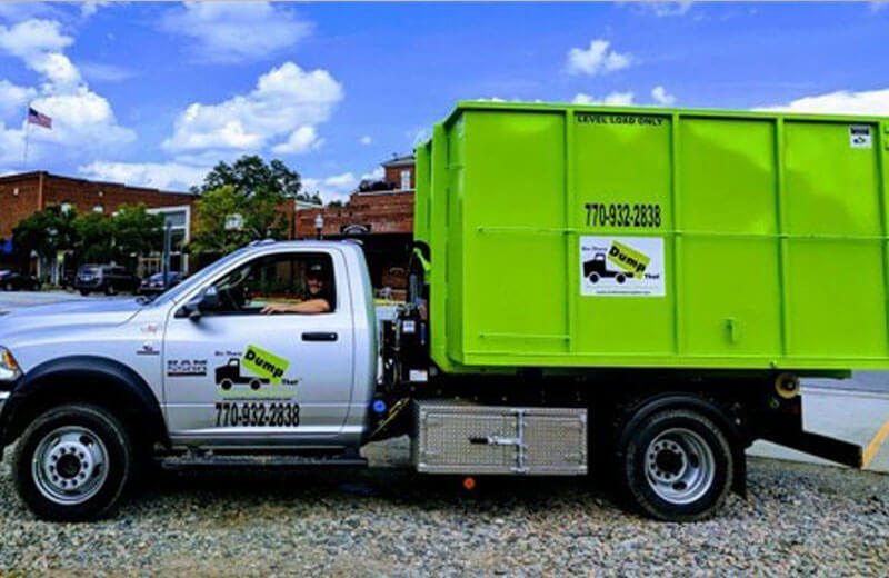 A green waste collection and junk hauling franchise truck parked with the driver sitting in the open cab door.