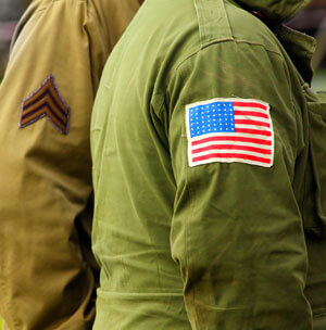 Two individuals in military uniforms, one with a u.s. flag patch and the other associated with a junk hauling franchise.