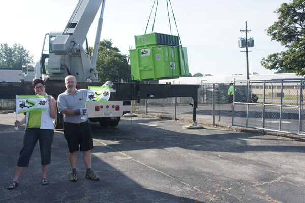 Two individuals standing next to a crane lifting a dumpster from a junk hauling franchise.